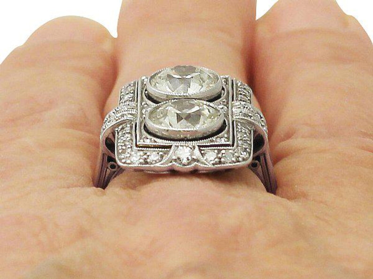 Close-up view on finger showing dual bezel-set round lab diamonds and intricate milgrain surface detail.