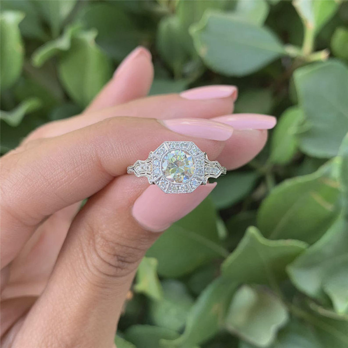 Outdoor natural light perspective of 2 CT round lab grown diamond octagon halo ring held between fingers.