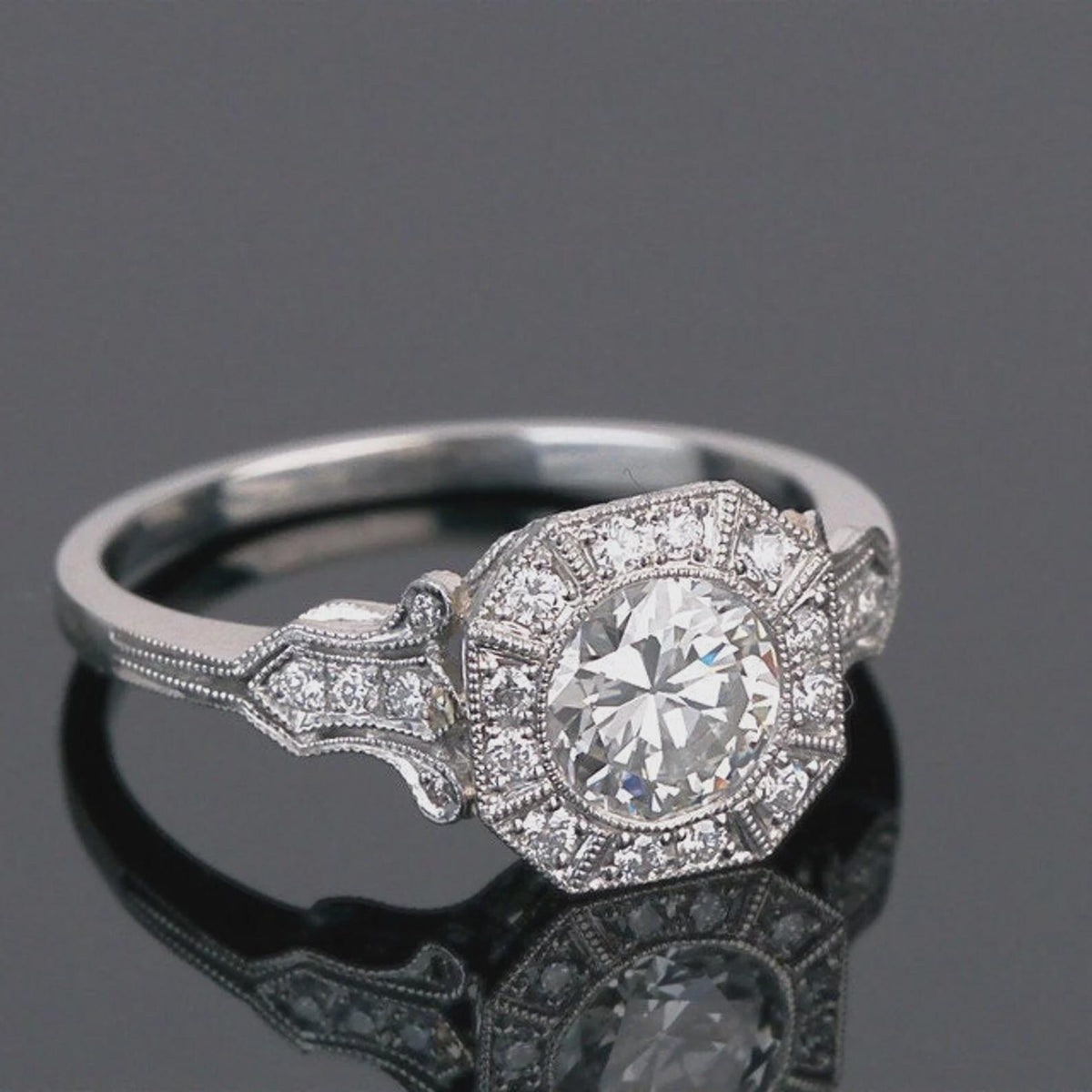 Studio shot on dark reflective surface showcasing geometric octagonal halo and round center lab diamond.