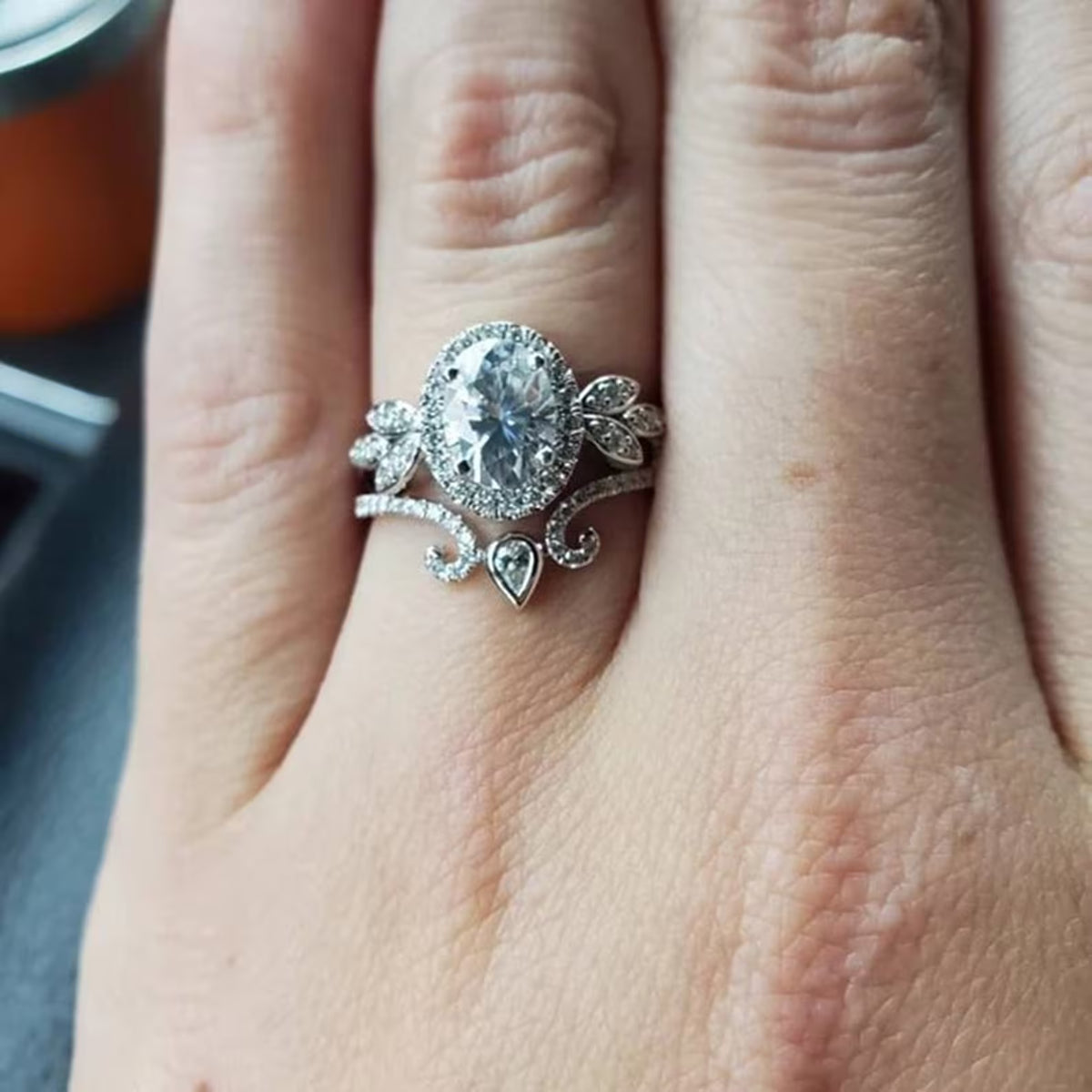Close-up finger view showing oval cut lab diamond halo ring paired with pear-accented tiara band.
