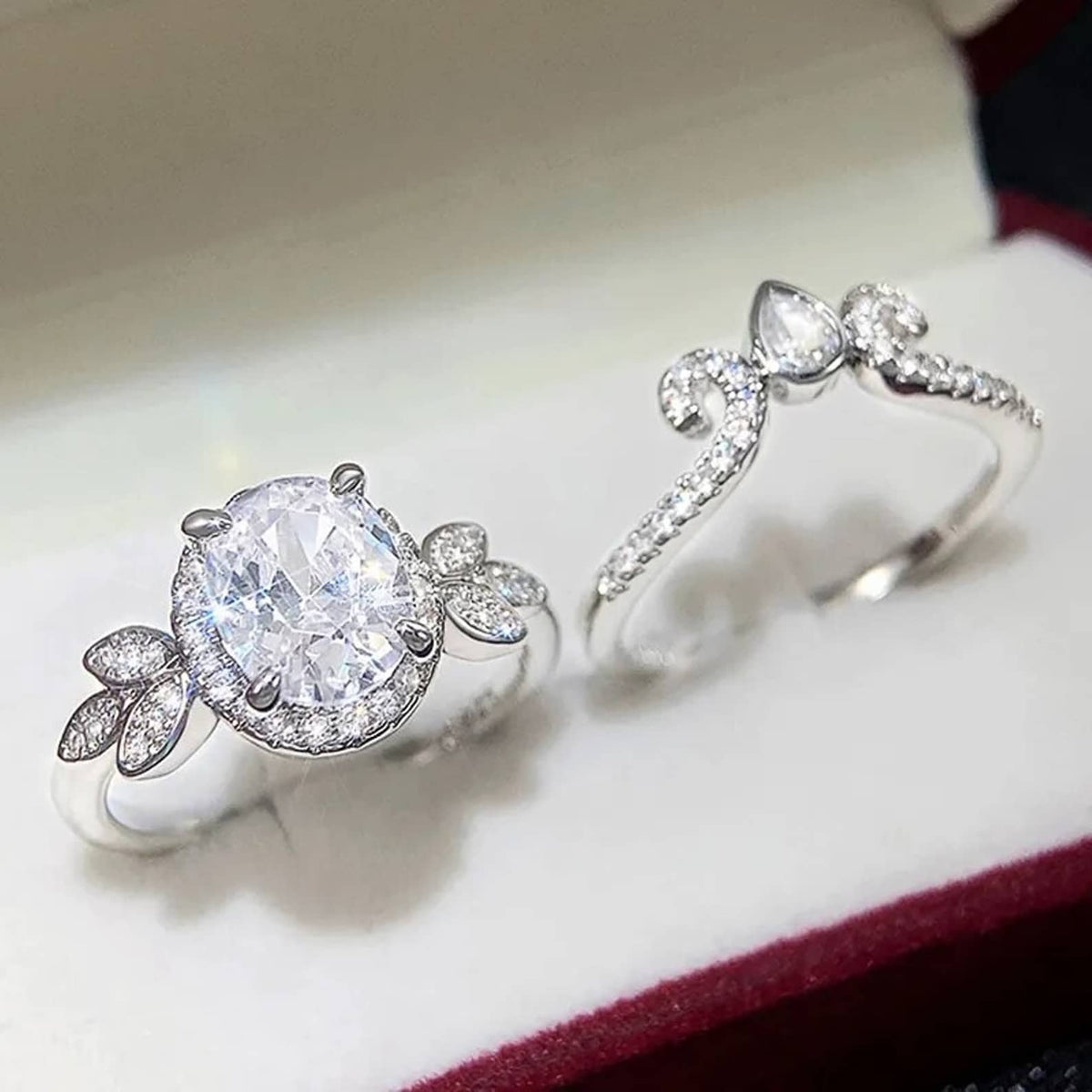 White ring box presentation displaying oval halo engagement ring alongside curved tiara wedding band.