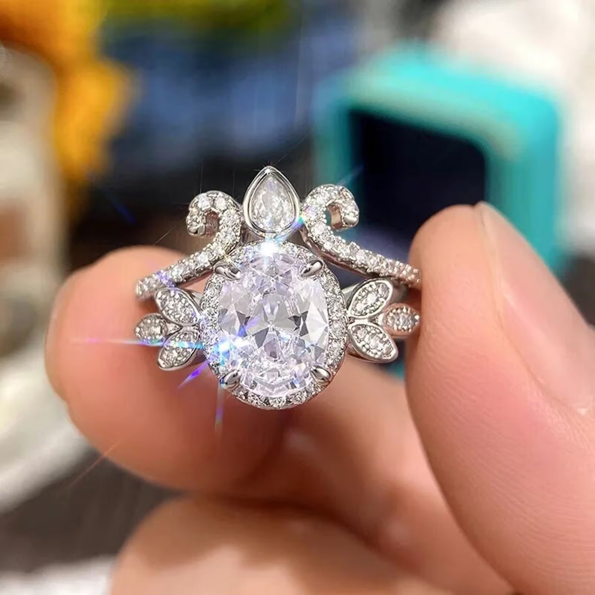 Close-up held between fingers showing brilliant light reflection on 2 CT oval halo ring and tiara set.