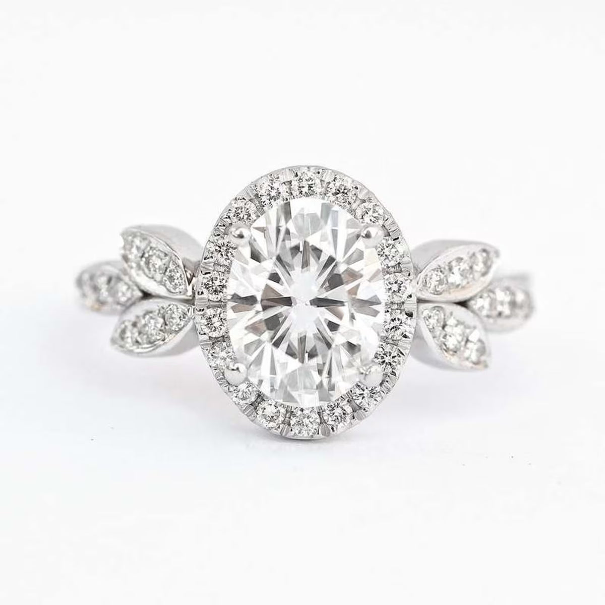 Isolated front view of 2 CT oval cut lab diamond halo engagement ring with leaf side accents on white background.