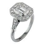 Perspective view of a 2 CT emerald cut lab-grown diamond engagement ring with an Art Deco octagonal halo and milgrain shoulders.