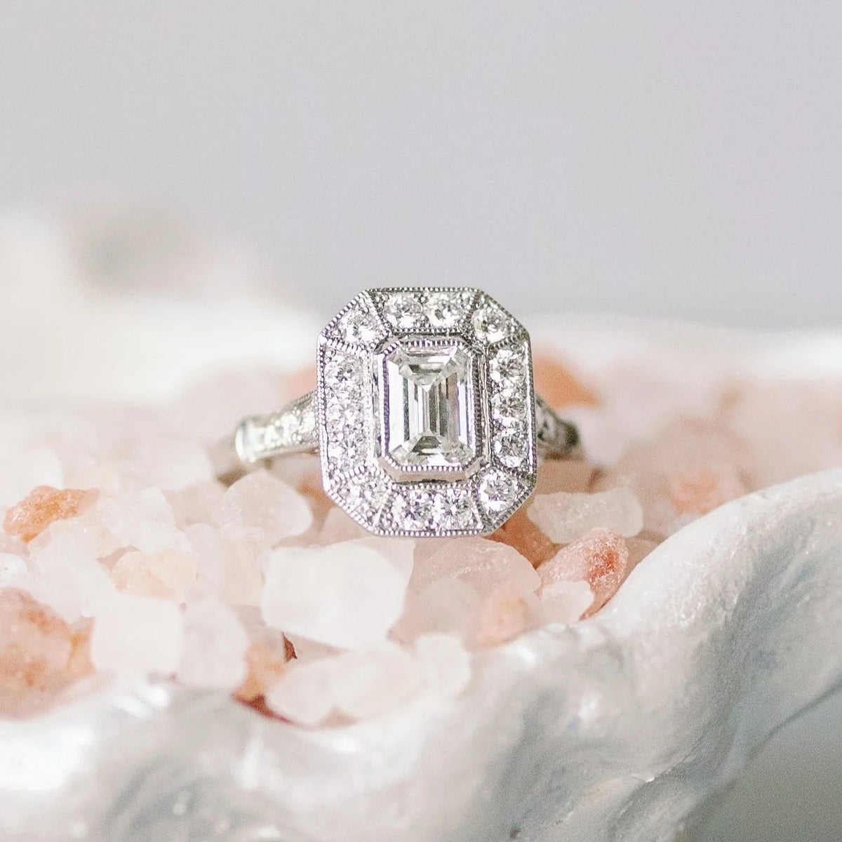 Styled display of a vintage 2 carat emerald cut lab diamond halo ring with intricate hand-engraved milgrain details.
