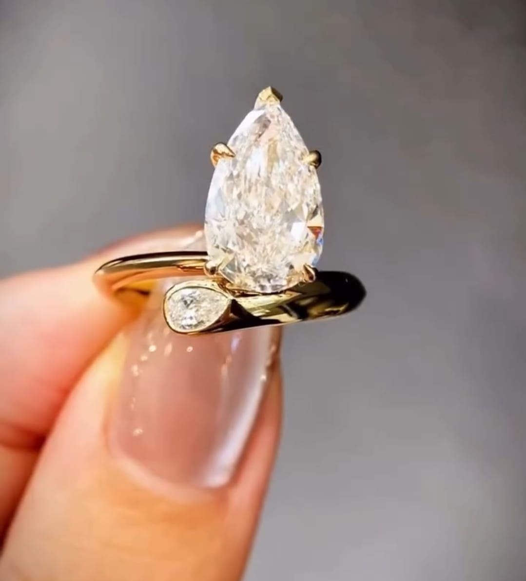 Front close-up view of a 3 CT pear cut lab grown diamond bypass engagement ring in 14K yellow gold held on finger.