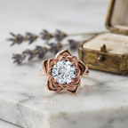 3ct round lab diamond blooming rose ring in rose gold resting on white marble next to a vintage ring box and lavender.