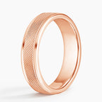 Angled view of rose gold men's wedding band featuring cross-hatch knurled texture and polished edges.