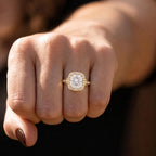 Close-up on hand showing a 4 carat cushion-cut diamond ring with a split shank and halo setting.