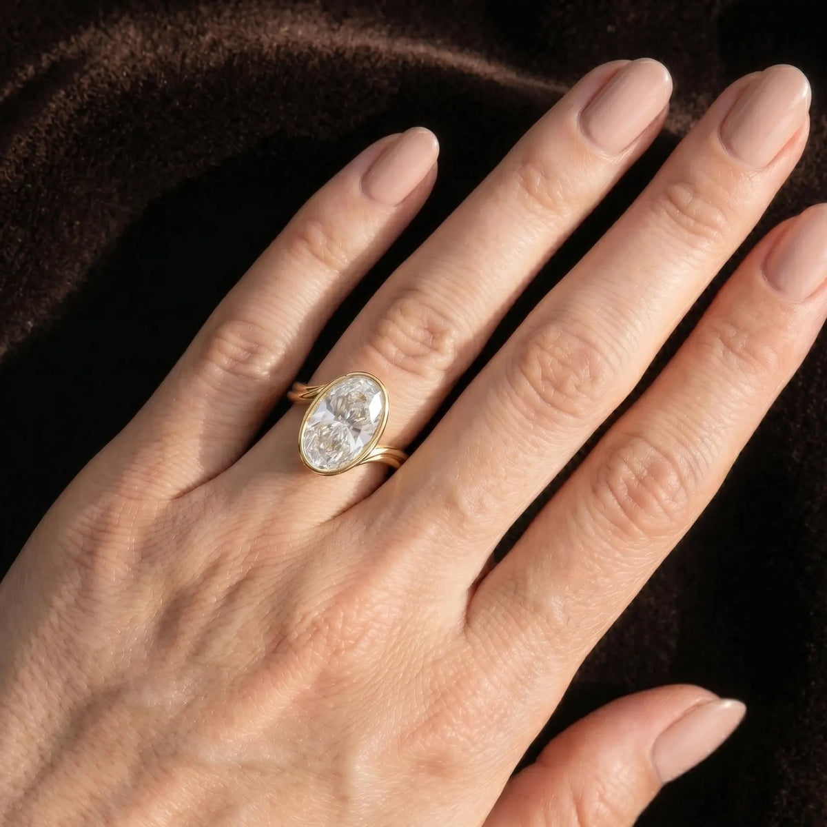 4 Carat oval cut lab grown diamond bezel engagement ring in yellow gold worn on hand.