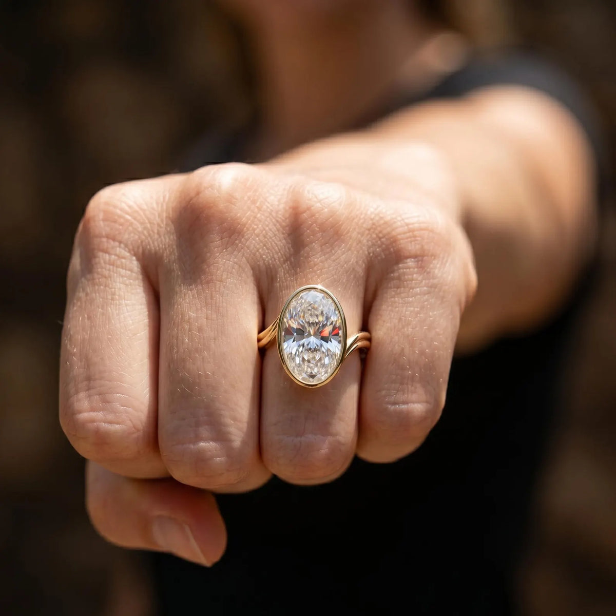 Front view of 4 CT oval lab diamond bezel ring with bypass band on finger.