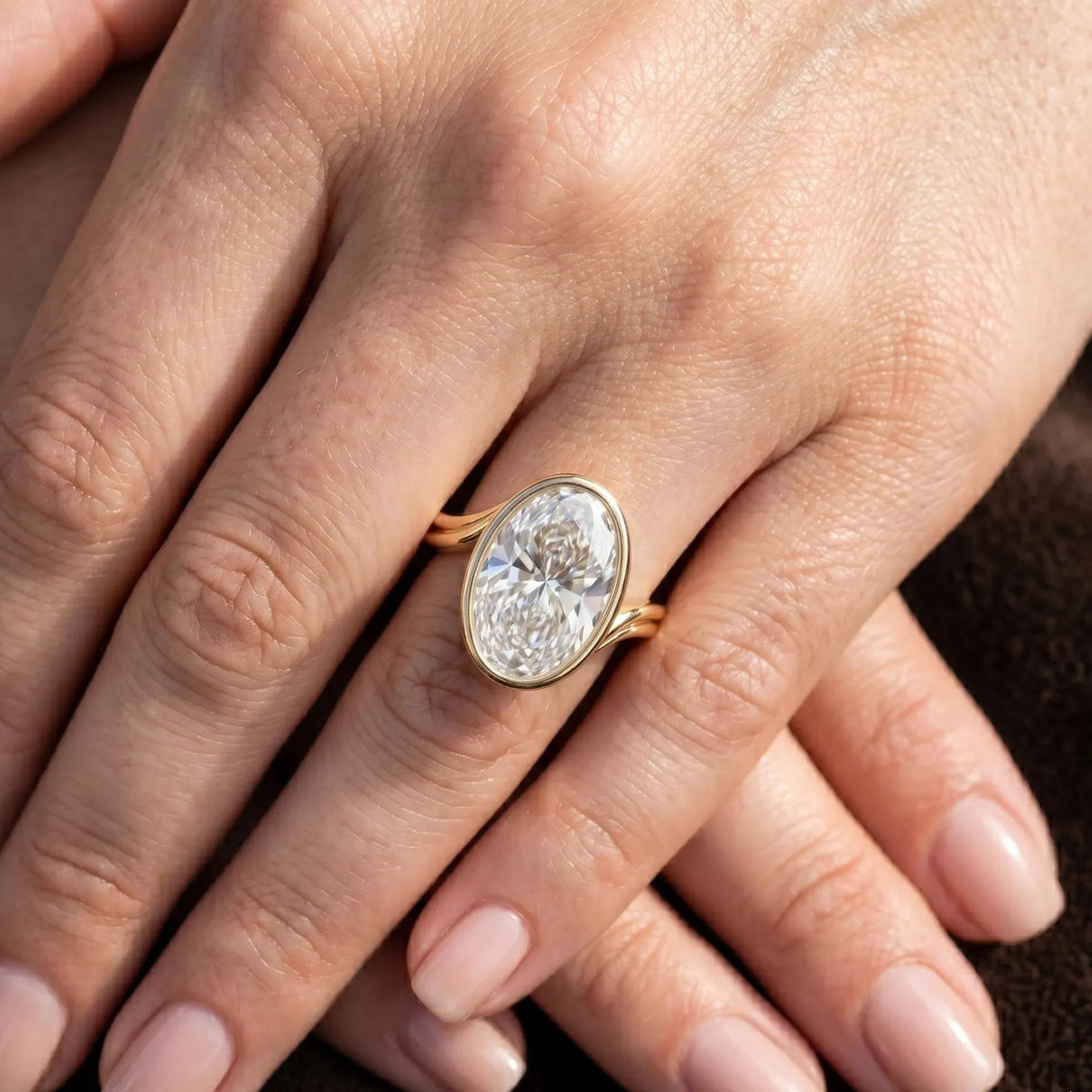 Elegant 4 carat oval lab diamond bezel engagement ring shown on crossed hands.
