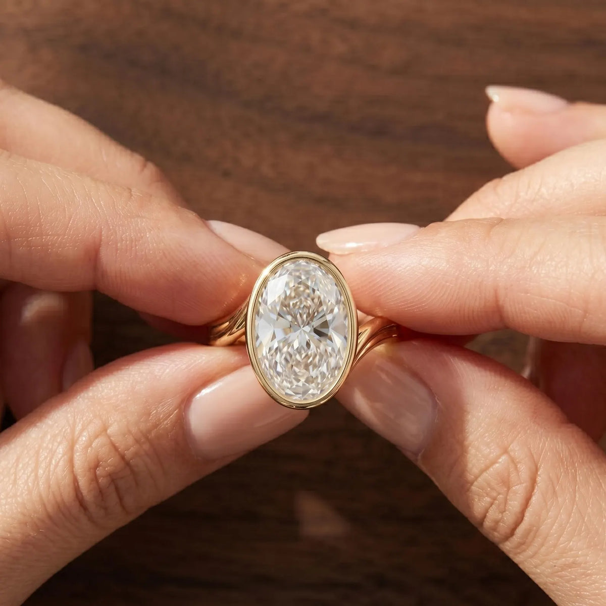Hands holding a 4 carat oval lab grown diamond bezel ring with curved bypass band.
