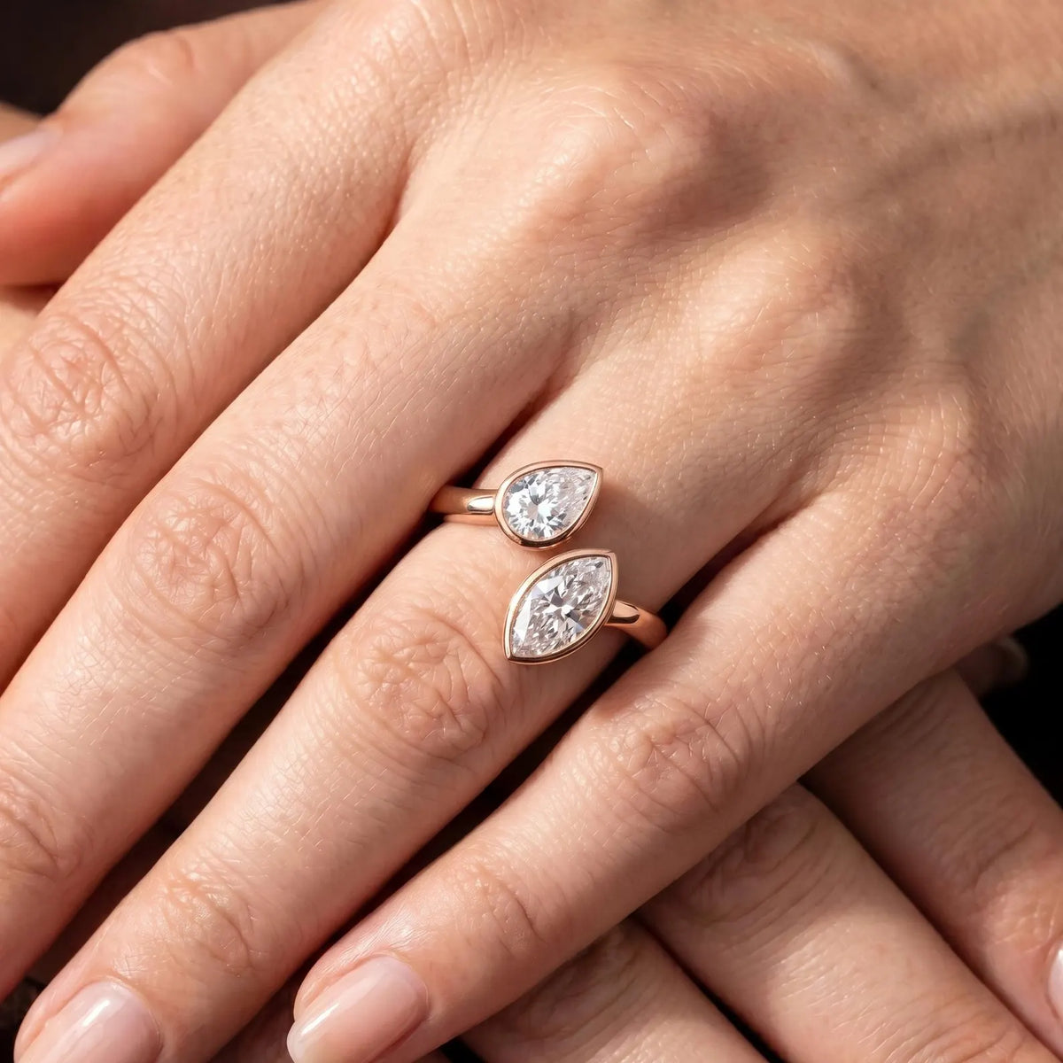 Pear and marquise cut lab grown diamond Toi et Moi bezel ring in rose gold worn on hand.