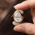 Hand holding a 3 carat pear cut lab diamond bezel ring over dark leather background.