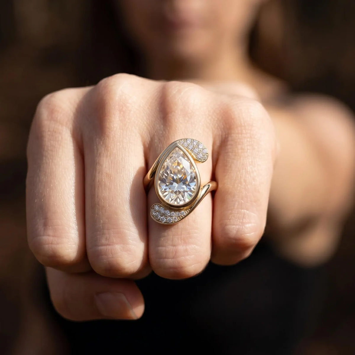 Front view fist shot wearing 3 CT pear cut lab grown diamond bezel bypass ring.