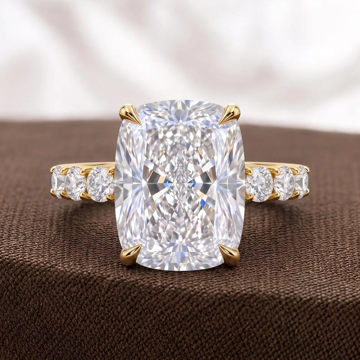 Front view of 4 CT elongated cushion cut diamond ring sitting on textured brown fabric.