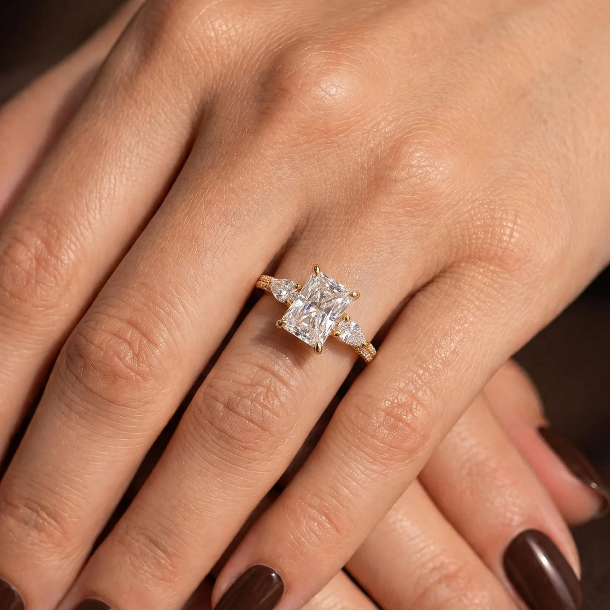 Top view of a 3 CT radiant cut three-stone lab grown diamond engagement ring worn on finger.