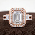 Top-down macro view of 3 carat emerald cut lab grown diamond ring with halo setting and baguette side stones in rose gold.
