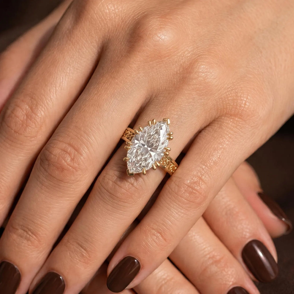 On-hand view of a 3 CT marquise cut lab grown diamond engagement ring with engraved yellow gold filigree band.