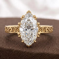 Frontal display of a 3 carat marquise cut lab grown diamond ring with intricate antique scrollwork band on brown fabric.