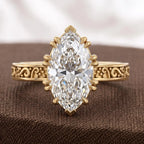 Frontal display of a 3 carat marquise cut lab grown diamond ring with intricate antique scrollwork band on brown fabric.