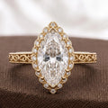 Flat lay photo of a 3.0 CT marquise cut lab diamond vintage halo ring with engraved shank on brown fabric background.