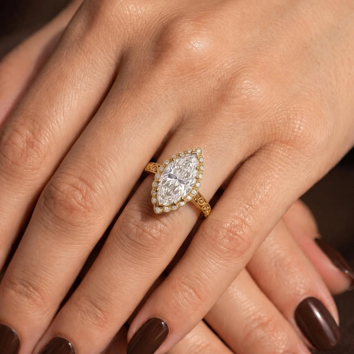 Aesthetic top-down view of a hand wearing a 3 carat marquise lab-grown diamond halo ring with detailed yellow gold scrollwork.
