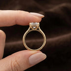 Side profile view of a 4 CT emerald cut lab diamond solitaire ring held between fingers showing open cathedral setting in yellow gold.