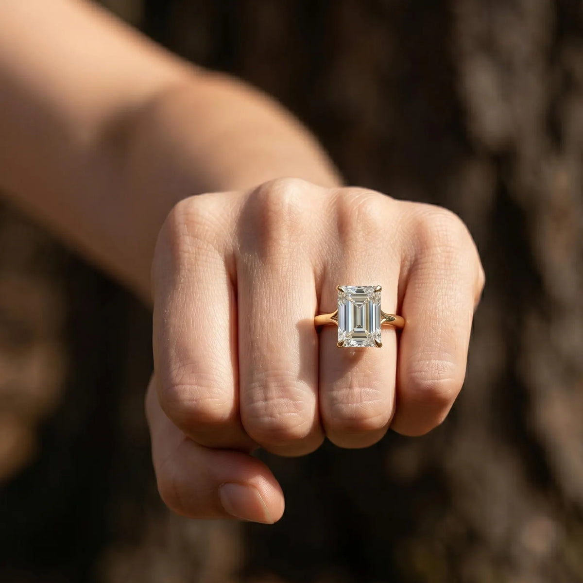 Front view of a 4 carat emerald cut lab grown diamond engagement ring worn on hand outdoors.