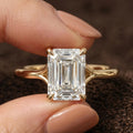 Direct front macro shot of a 4 carat emerald cut lab diamond solitaire engagement ring held between fingers.