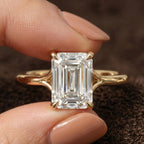 Direct front macro shot of a 4 carat emerald cut lab diamond solitaire engagement ring held between fingers.