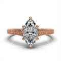 Top view of a rose gold hand-engraved scrollwork engagement ring with a 3 carat marquise lab-grown diamond.