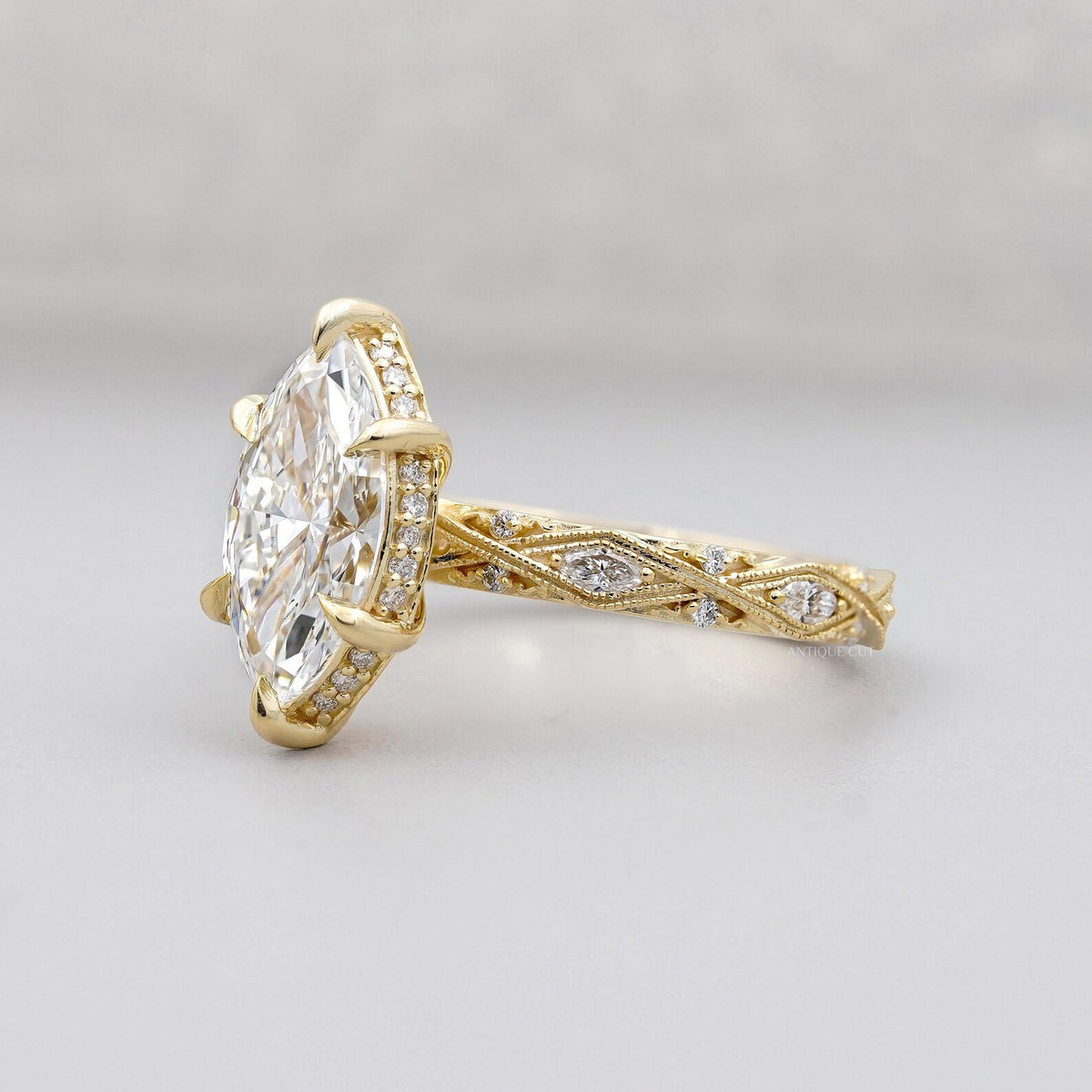 Side profile view of a 3 carat marquise lab diamond ring highlighting the textured milgrain lattice band and diamond-encrusted basket.