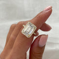 4 Carat emerald cut lab grown diamond halo engagement ring with pavé band in yellow gold worn on finger.