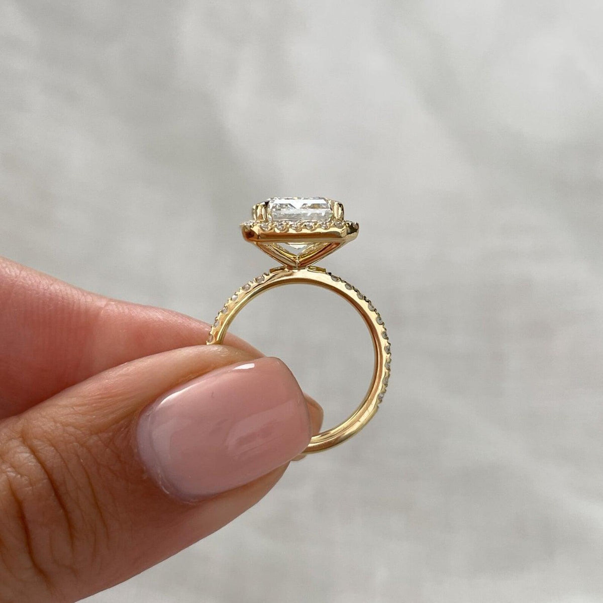 Side profile view of a 4 carat emerald cut lab diamond halo ring showcasing the yellow gold basket setting and band.