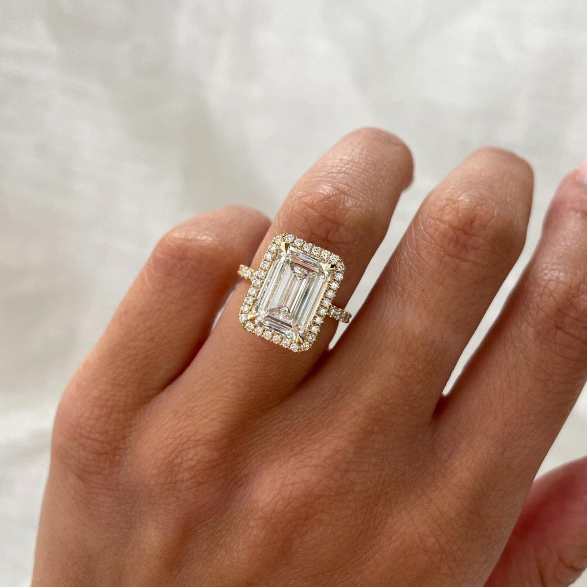 Top-down view of a 4 CT step-cut emerald lab grown diamond engagement ring with micro-pavé halo on hand.