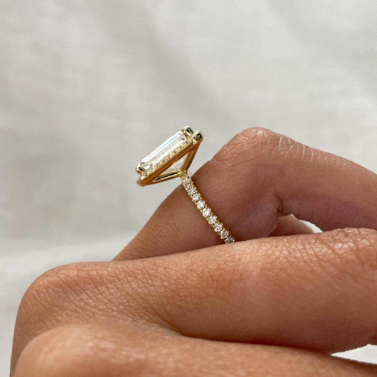 Close-up side angle of a yellow gold lab grown emerald cut diamond ring highlighting the thin pavé diamond band.