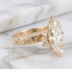 Side angle view of 4 carat marquise cut lab grown diamond ring featuring vintage scroll engraving on yellow gold band.