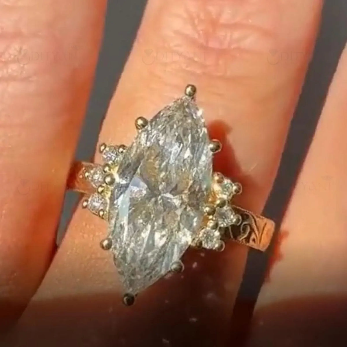 Top-down view of a 4 carat marquise cut lab grown diamond ring with an engraved band worn on a finger.