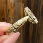 Close-up of yellow gold hand-engraved floral shank and milgrain edge gallery on an oval lab diamond ring.