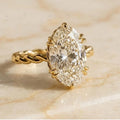 3 carat oval cut lab grown diamond solitaire ring with twisted rope band in yellow gold on marble surface.