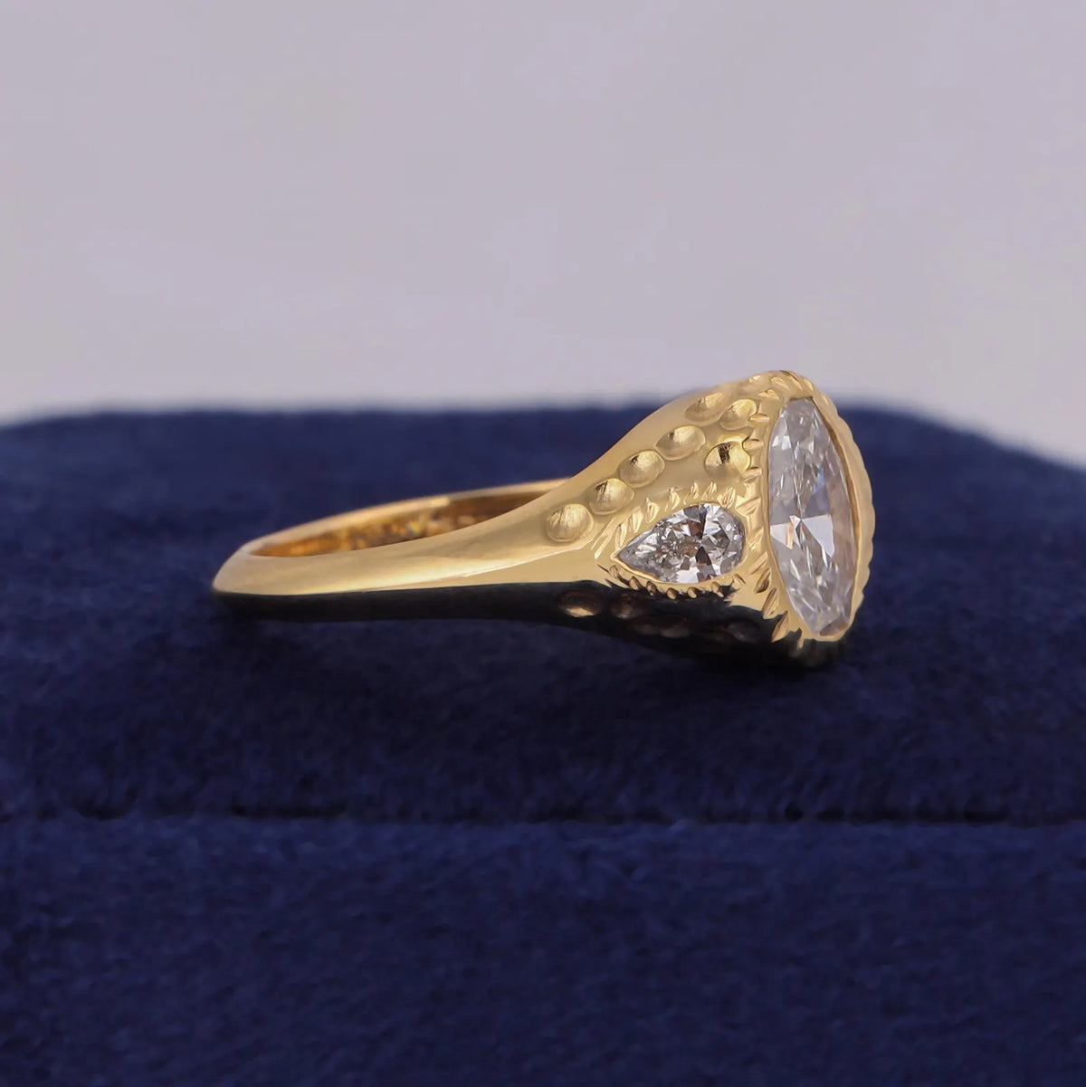 Side profile of wide 14K yellow gold signet ring featuring hammered texture and flush-set pear side diamond