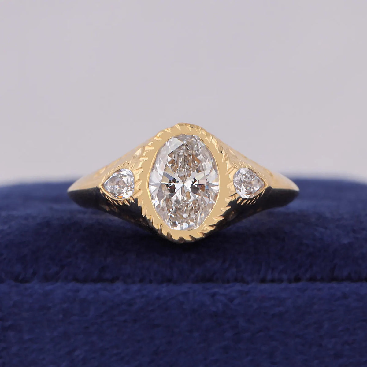 Front view of 3 carat oval lab diamond ring with star-carved bezel edge and twin pear side stones.