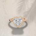 3ct heart cut lab grown diamond ring with a rose gold bezel setting on a neutral background