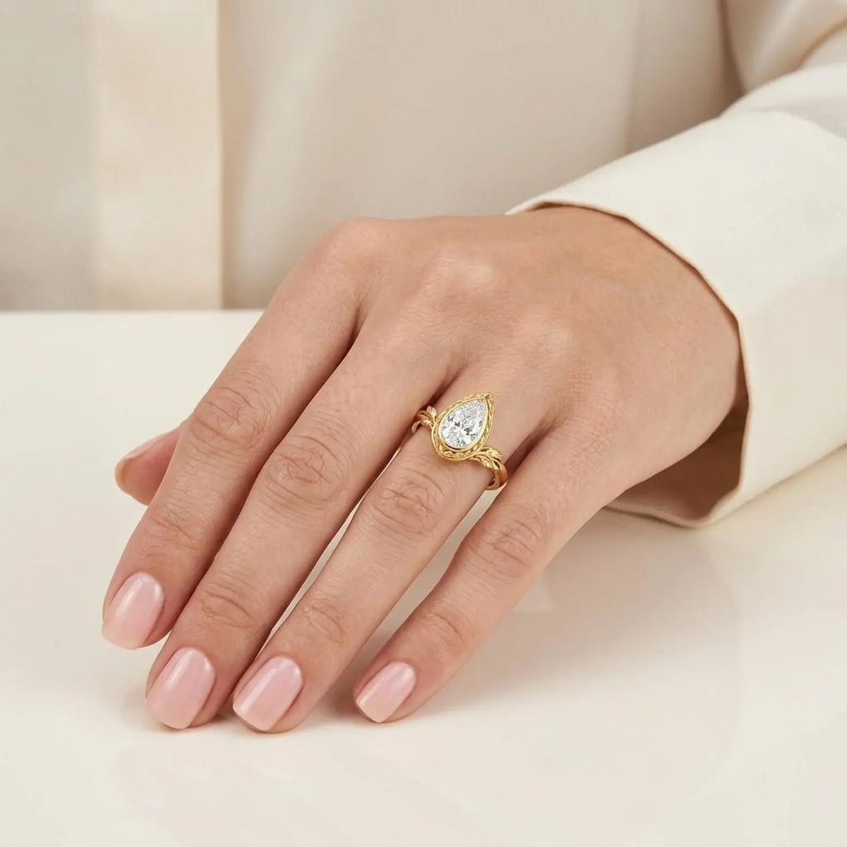 On-hand photo of 3 CT pear cut lab diamond engagement ring in yellow gold with leaf design.
