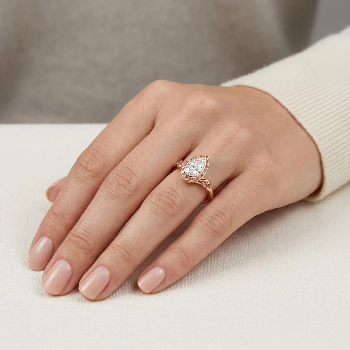 On-hand perspective of rose gold pear cut lab diamond engagement ring with organic leaf shoulders.