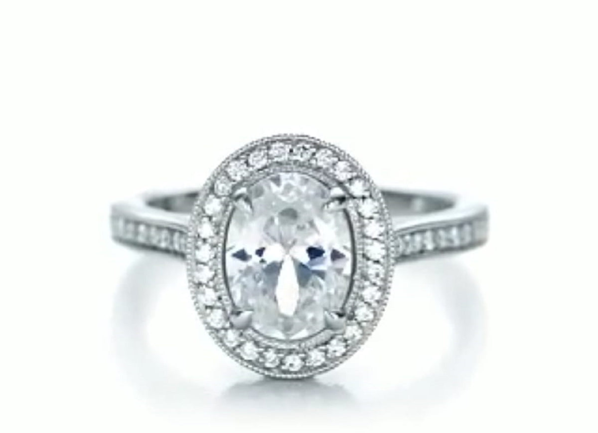 Frontal top-down view of a 3 CT oval cut lab grown diamond engagement ring with a milgrain-bordered halo and pavé band.