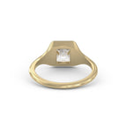 A yellow gold signet ring with a square bezel setting holding a clear, cushion-cut gemstone, shown on a plain white background.