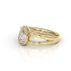 A yellow gold ring featuring a pear-cut diamond in a bezel setting, with a split shank band, shown on a clean white background with a soft reflection.